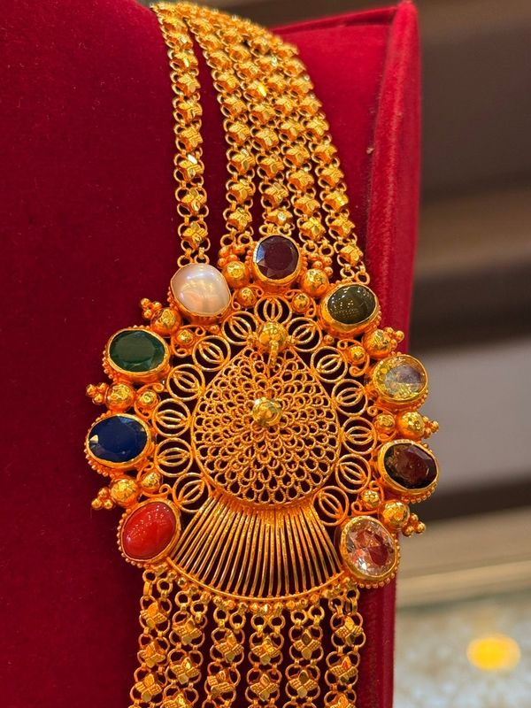 Chandrahaar necklace with an intricate round centrepiece and coloured stones on red velvet