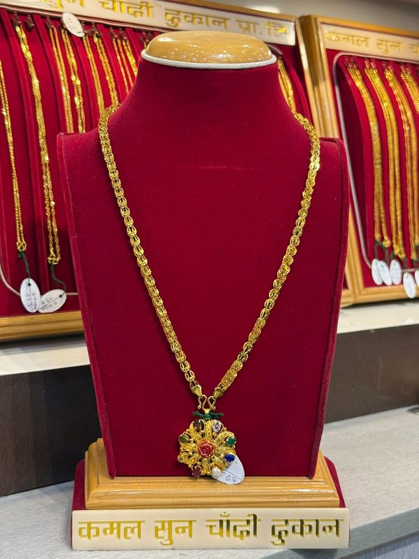Floral pendant with coloured details on a chain, displayed on a red necklace stand