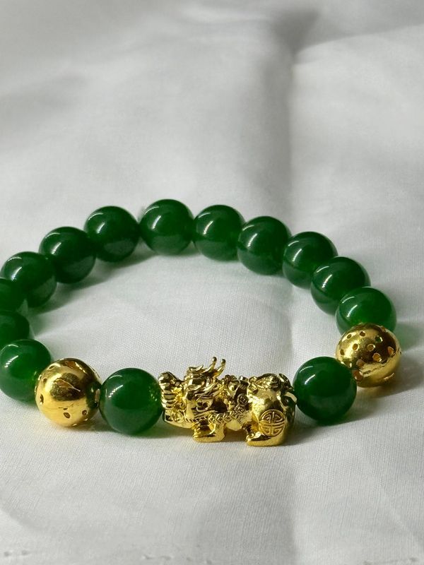 Green beaded bracelet with gold-coloured sculptural details on light fabric